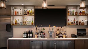 Un coin bar avec des étagères remplies de bouteilles d’alcool, un mini-bar et un téléviseur à écran plat.