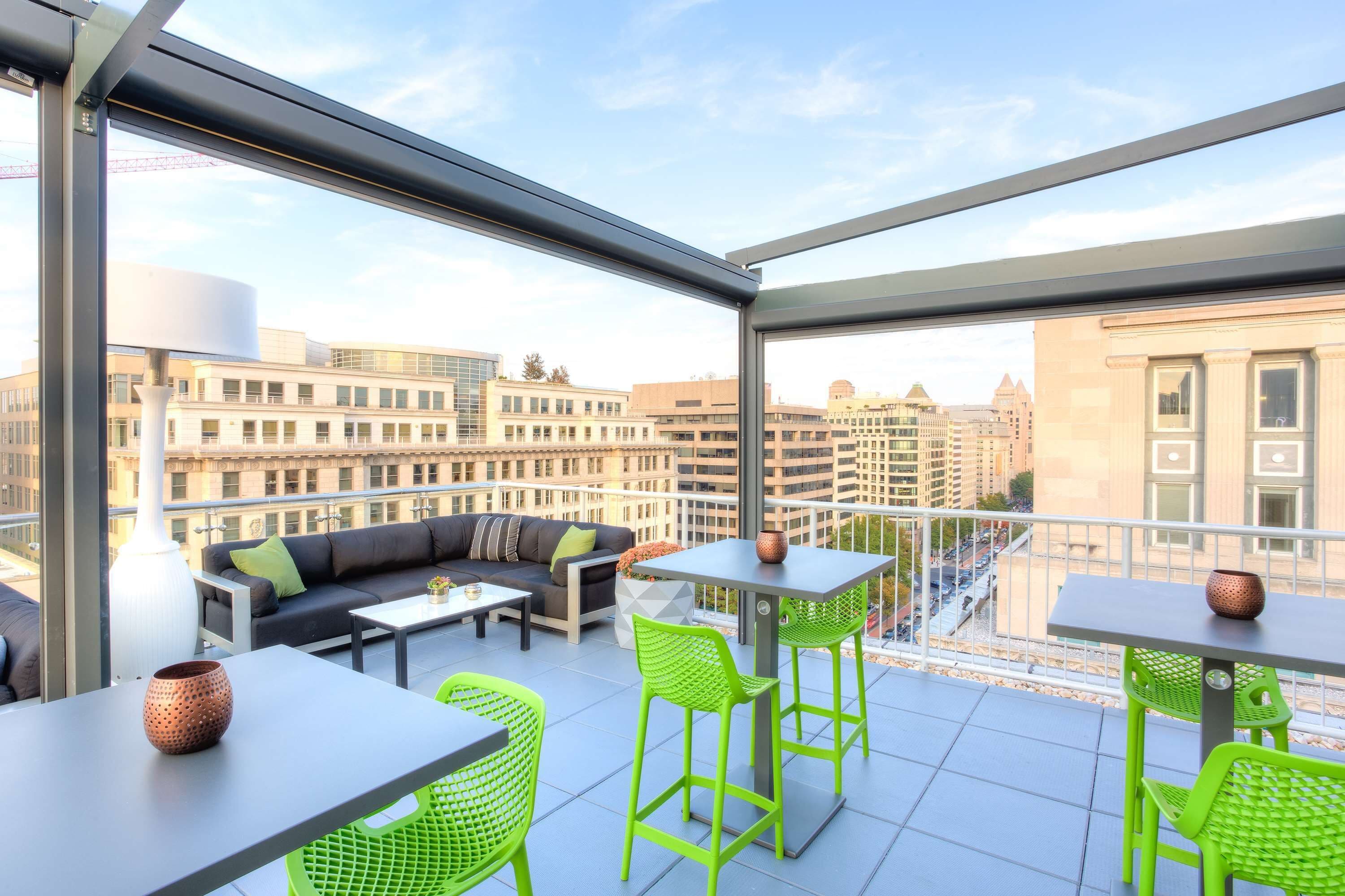 A modern outdoor balcony with a sofa, chairs, and tables, offering a city view.