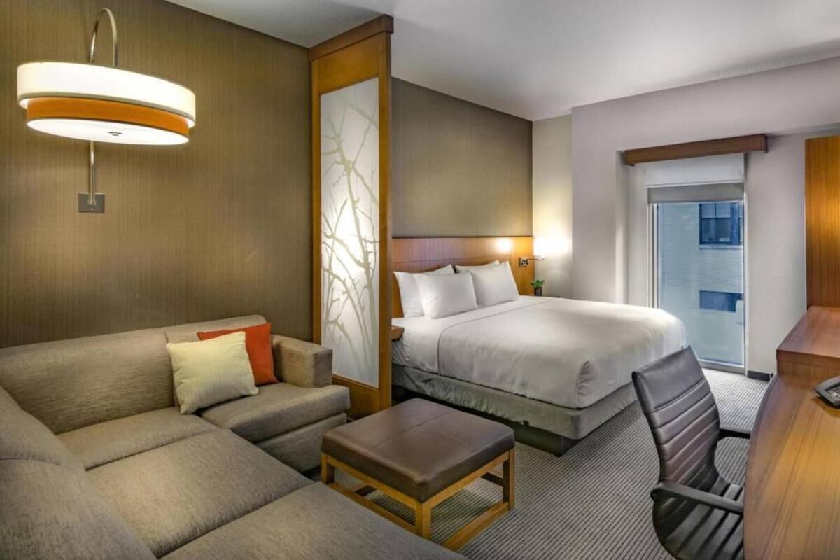 A hotel room with a bed, a sofa, a desk, and a chair.