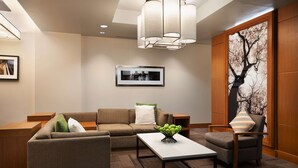 Un salon moderne avec un canapé, un fauteuil, une table basse et un grand tableau représentant un arbre accroché au mur.