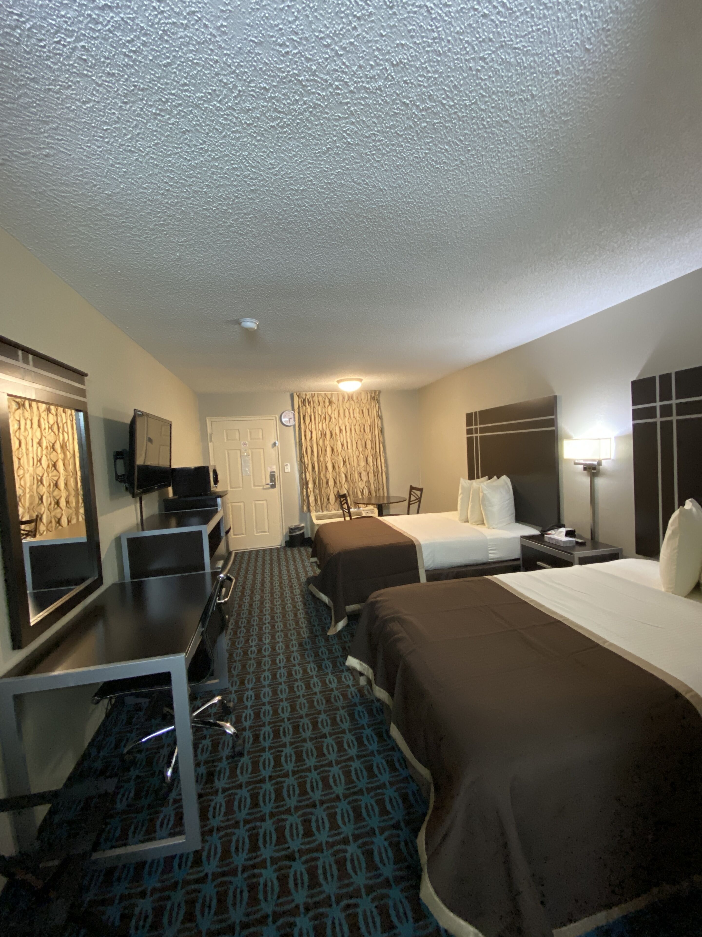 A hotel room with two beds, a desk, a chair, a television, and a bathroom.