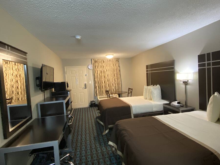 A hotel room with two beds, a desk, a chair, a television, and a bathroom.
