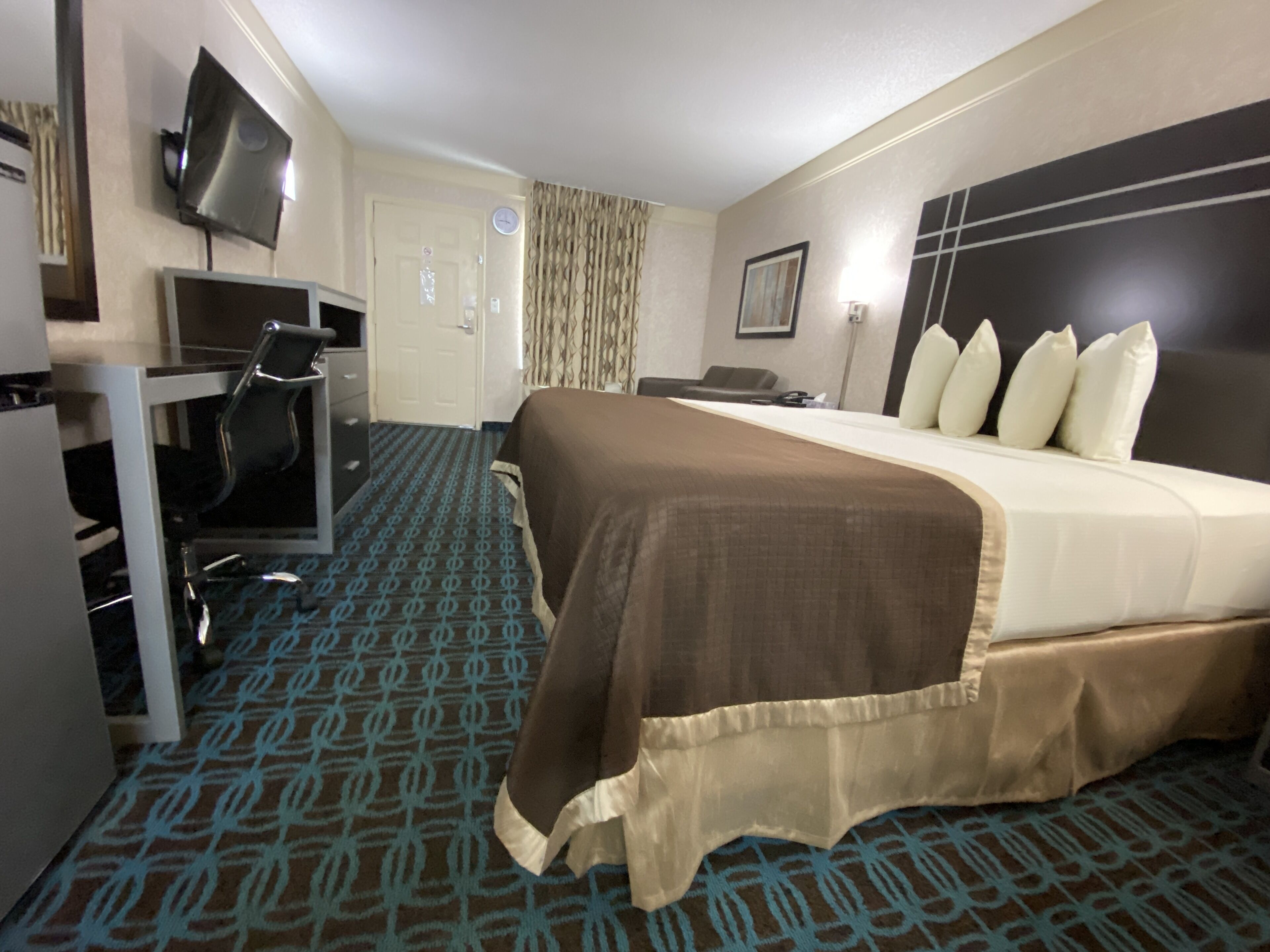 A hotel room with a bed, a desk with a chair, a television, and a door.