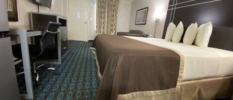 A hotel room with a bed, a desk with a chair, a television, and a door.