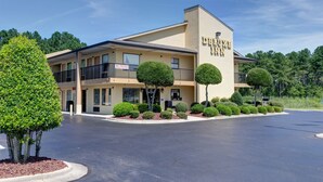 A hotel with a 'No Trucks' sign, a covered parking area, and neatly trimmed trees in front. - Deluxe Inn Fayetteville - I-95 Exit 49 (Fayetteville)