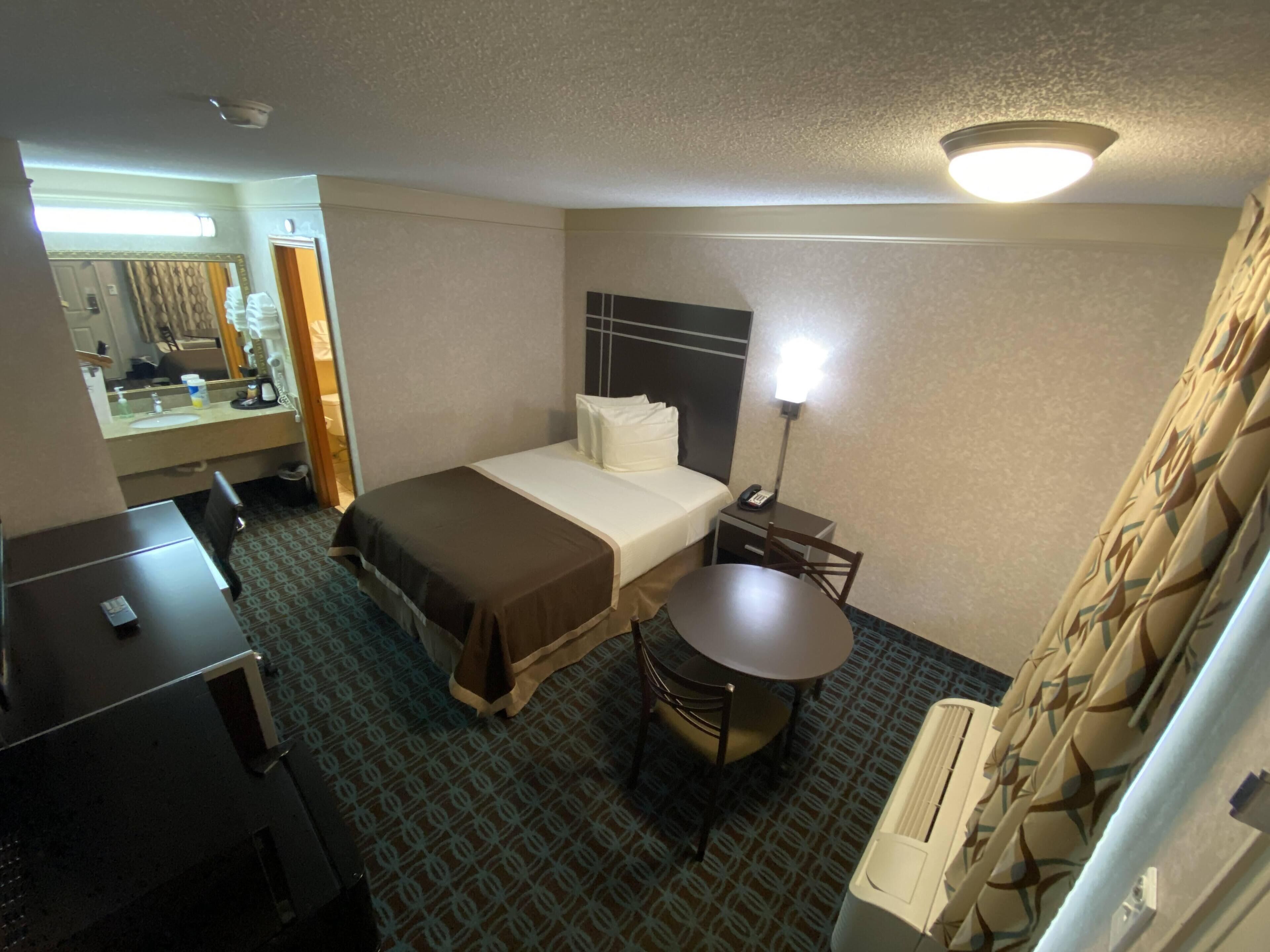 A hotel room with a bed, bedside table, desk, chair, and a small round table.