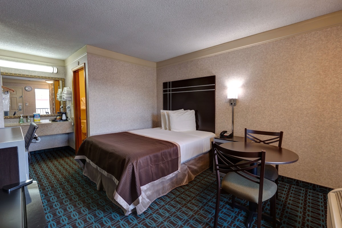 A hotel room with a bed, a desk, a chair, and a small table.