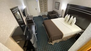A hotel room with a bed, a desk, a chair, a television, and a door. - Deluxe Inn Fayetteville - I-95 Exit 49 (Fayetteville)