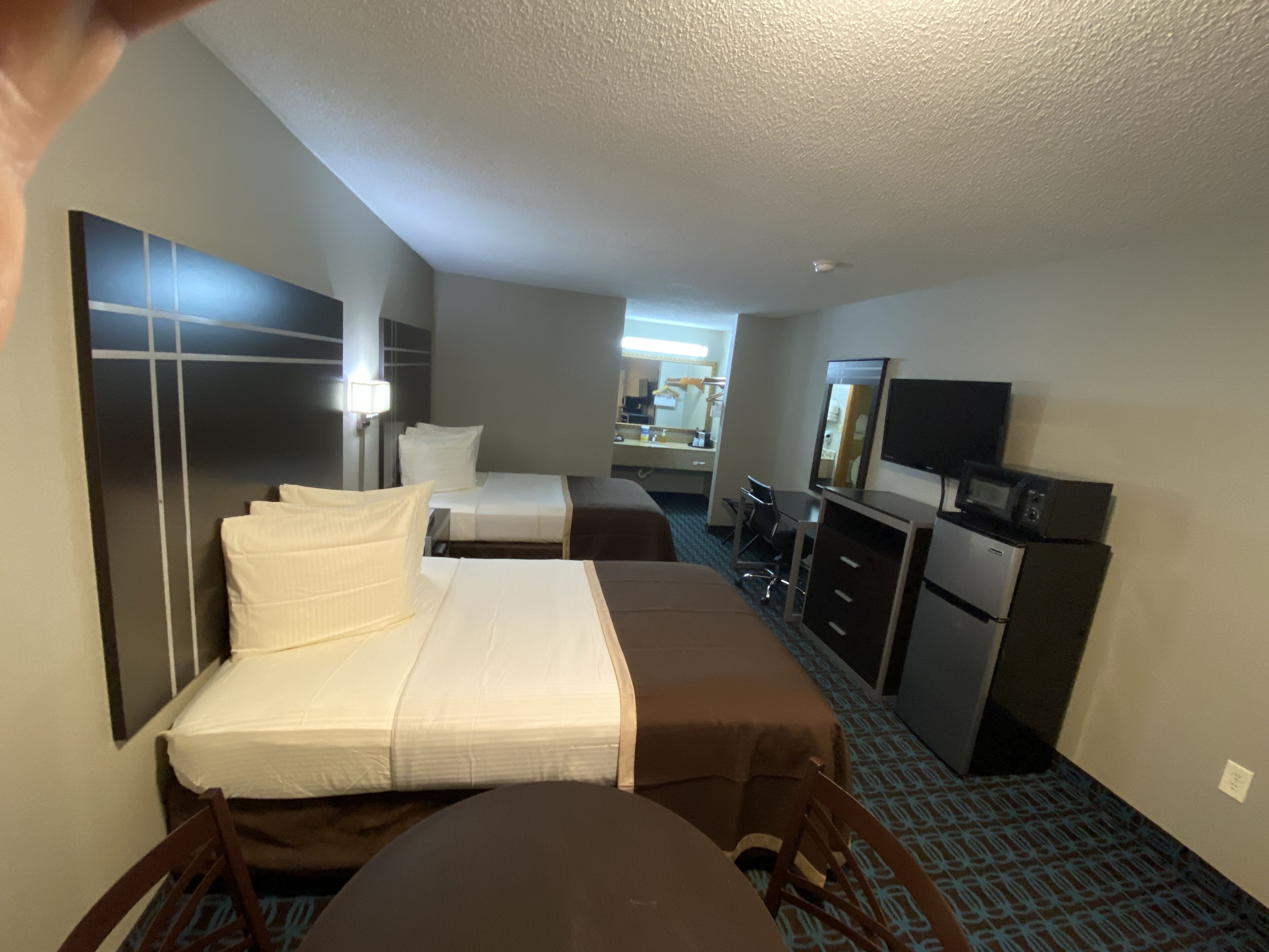 A hotel room with two beds, a desk, a chair, a television, and a dresser.