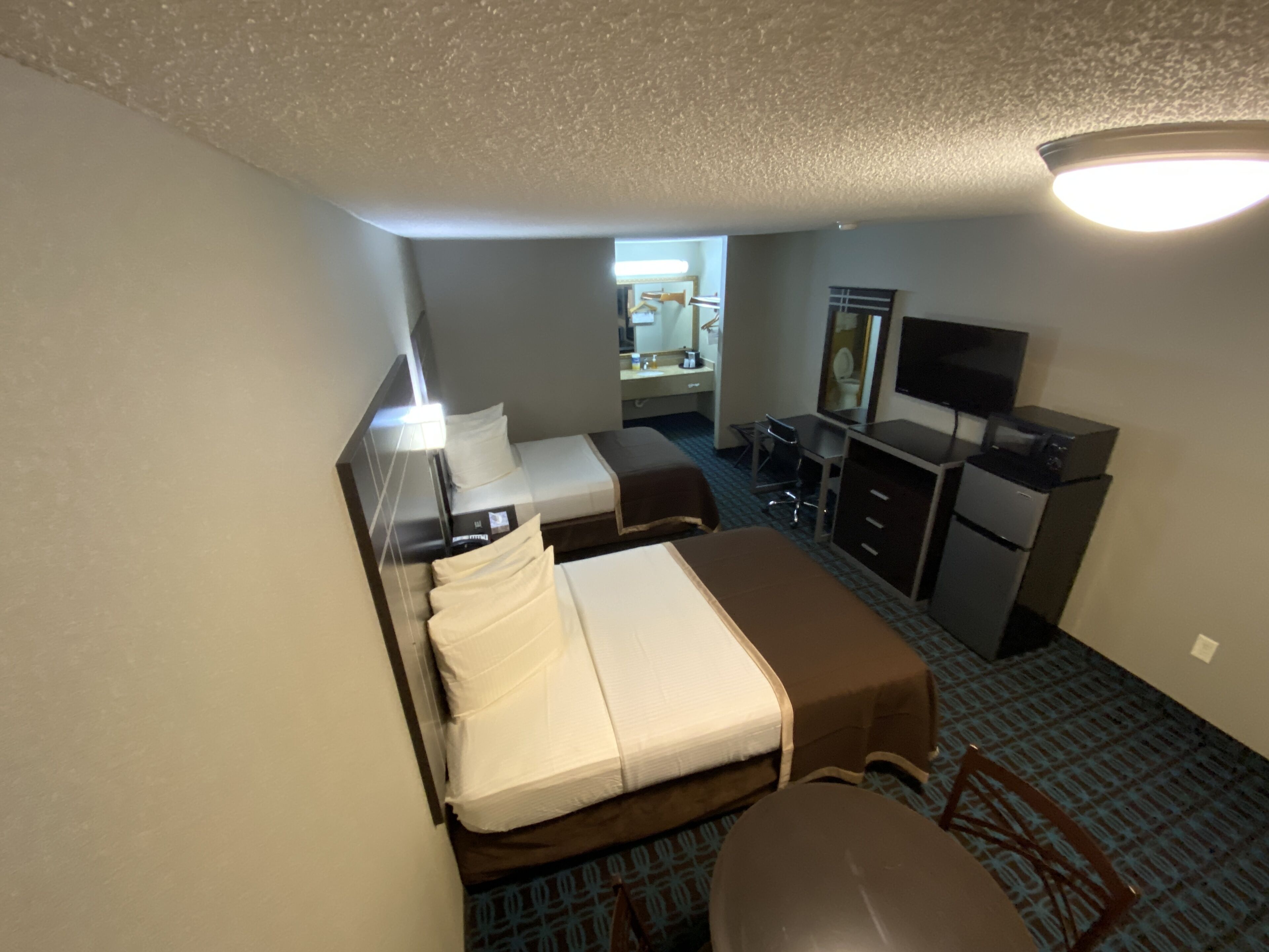 Habitación de hotel con dos camas, un escritorio, una silla, un televisor y un baño visible a través de una puerta abierta.