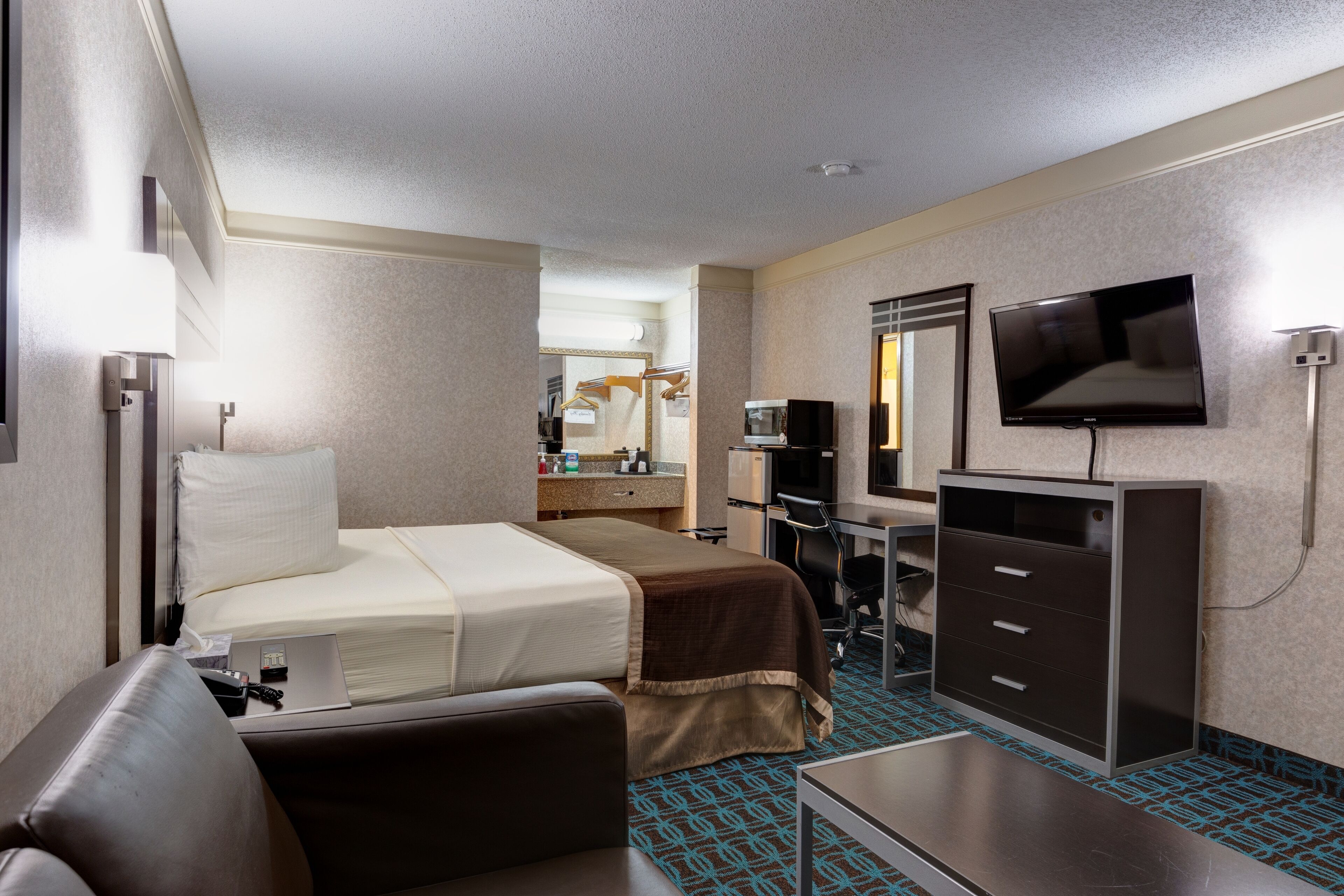 A hotel room with a bed, a desk, a television, and a wardrobe.
