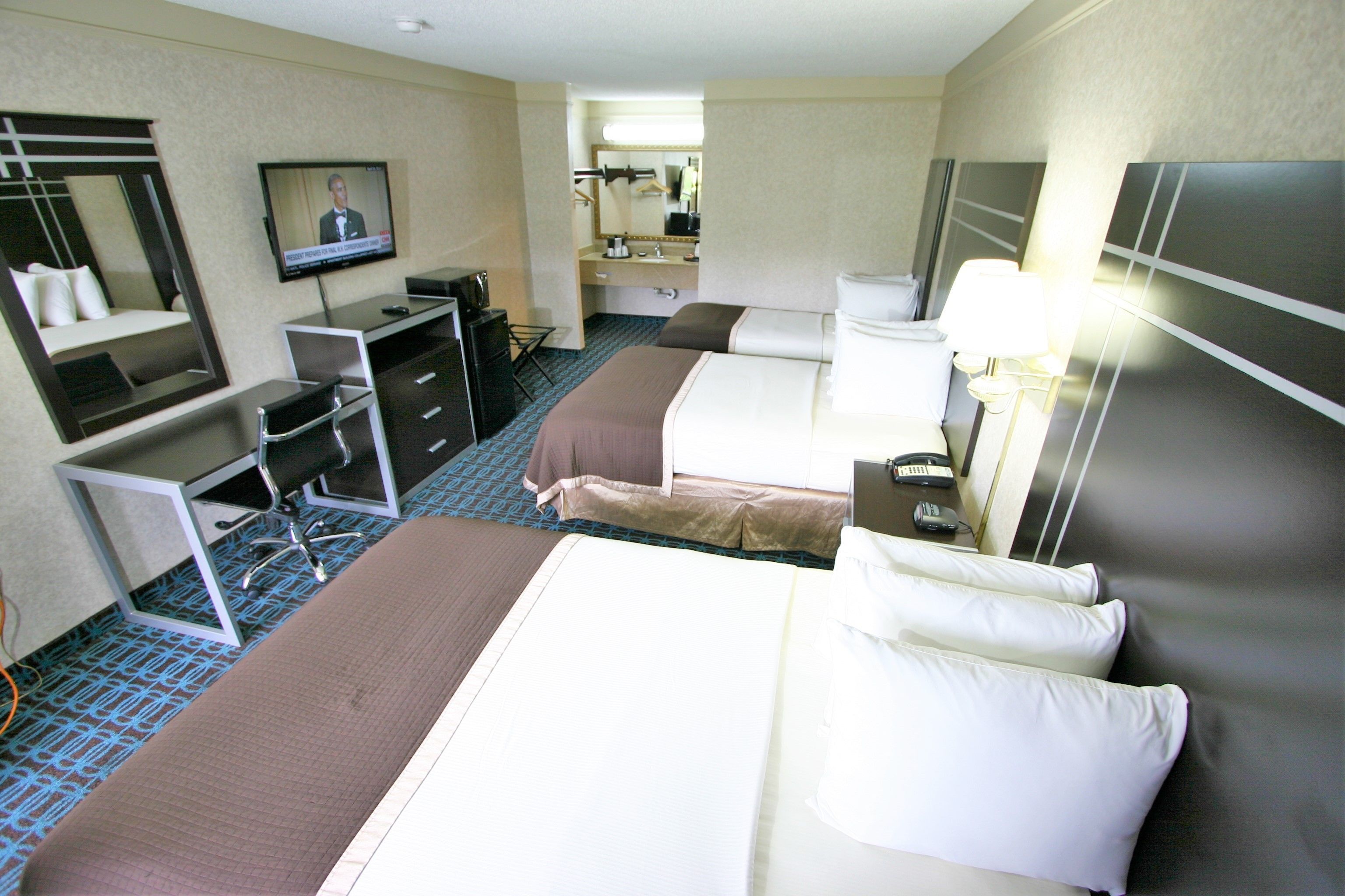 Habitación de hotel con dos camas, un escritorio, televisión, espejo y baño visible a través de una puerta abierta.
