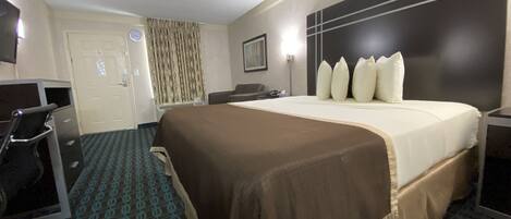 A hotel room with a bed, a desk, a chair, a television, and a door.