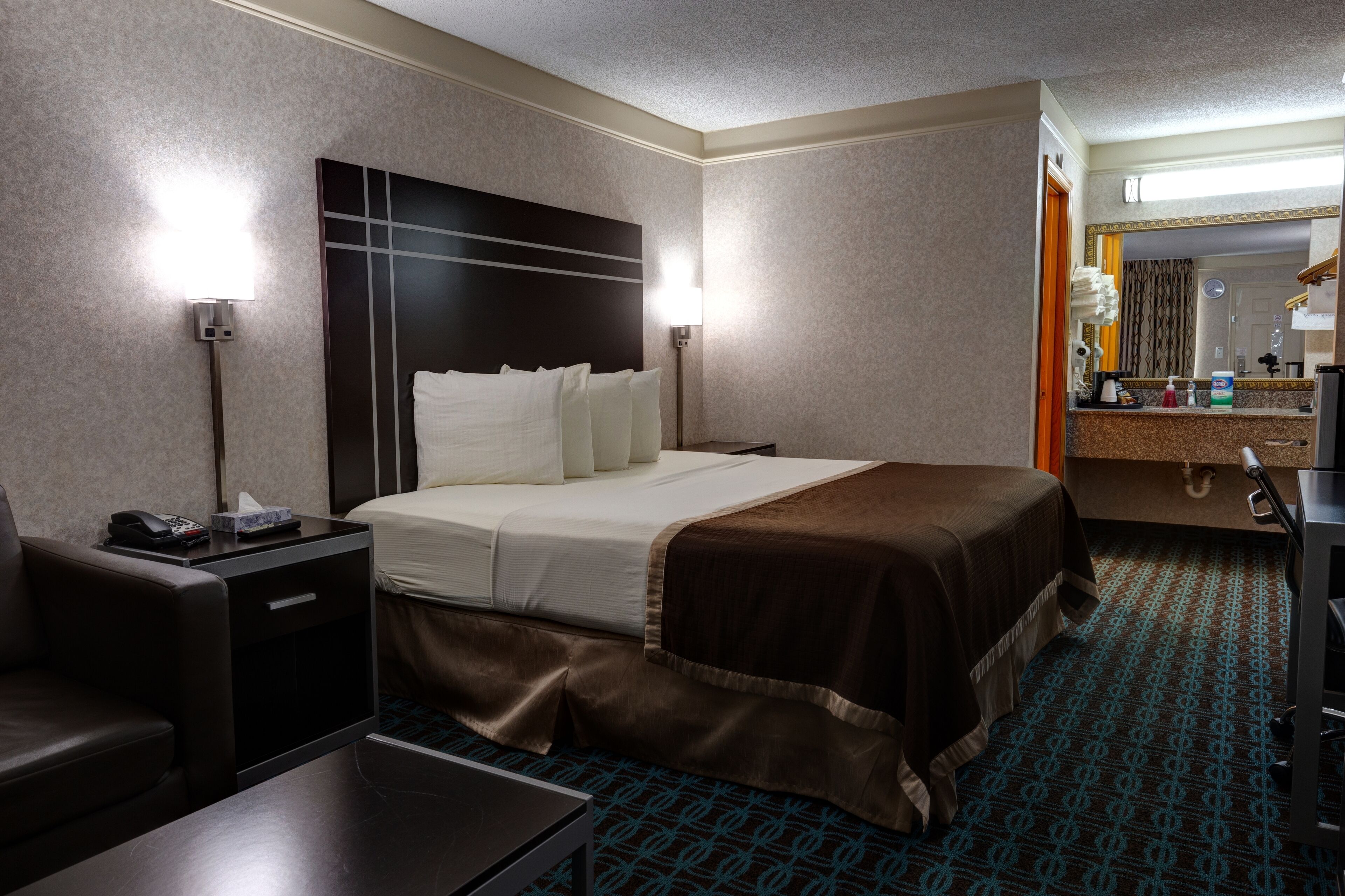 Ein Hotelzimmer mit Bett, Nachttischen, Schreibtisch, Spiegel und einem durchgegangene Tür einsehbaren Badezimmer.