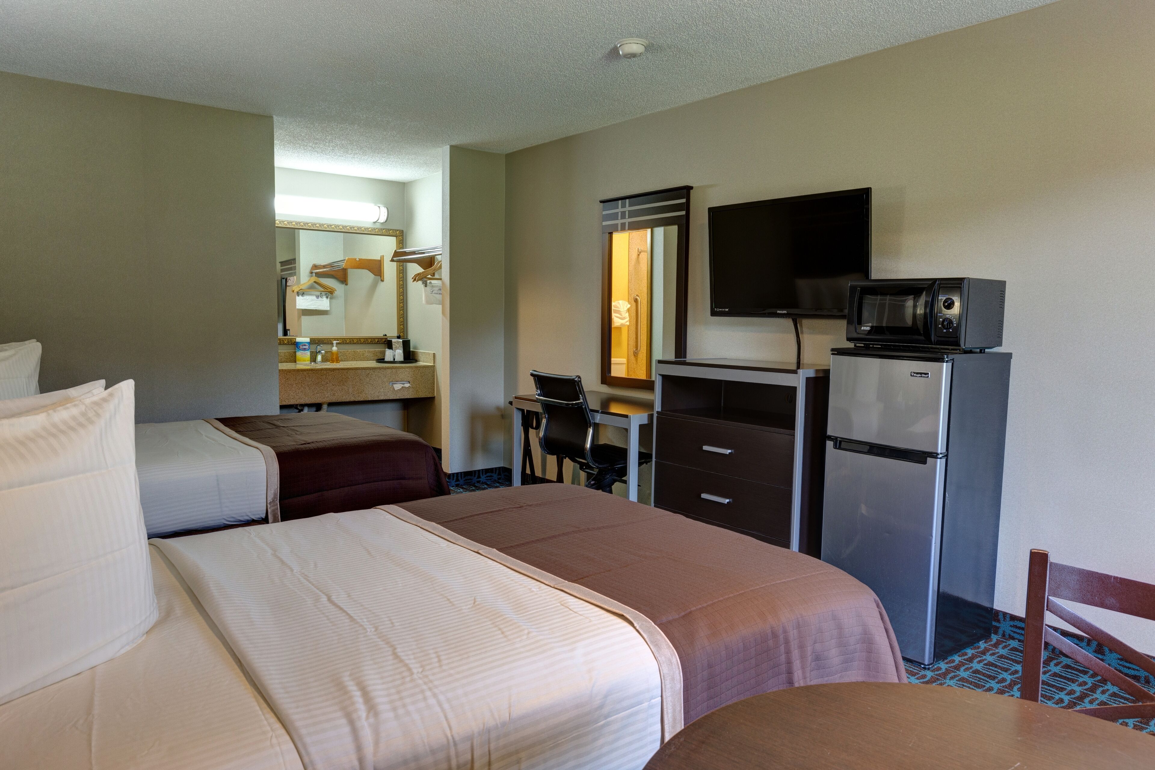 Una habitación de hotel con dos camas, un escritorio, una silla, un televisor, un refrigerador y un microondas.