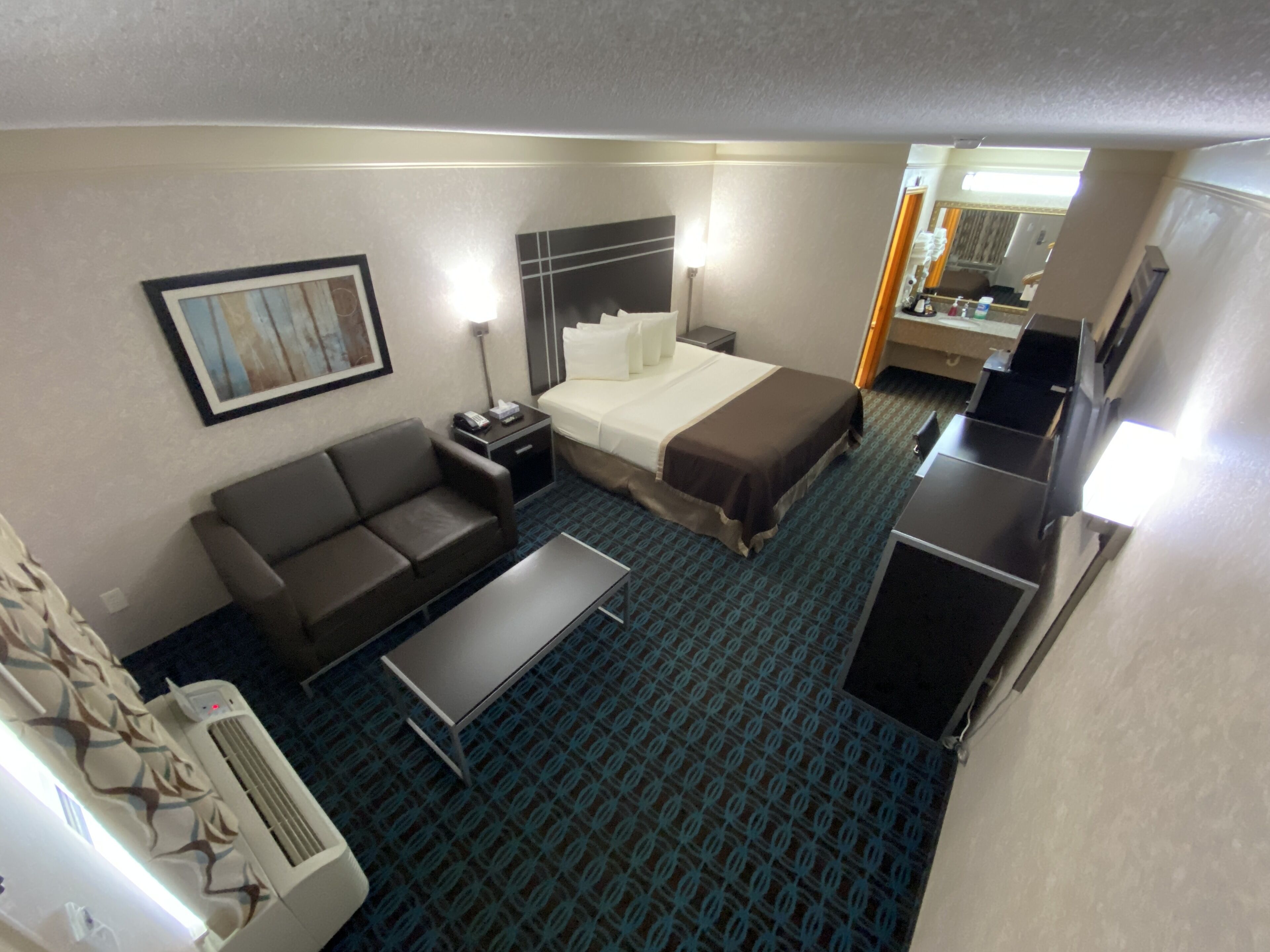 A hotel room with a bed, a sofa, a desk, and a kitchenette.