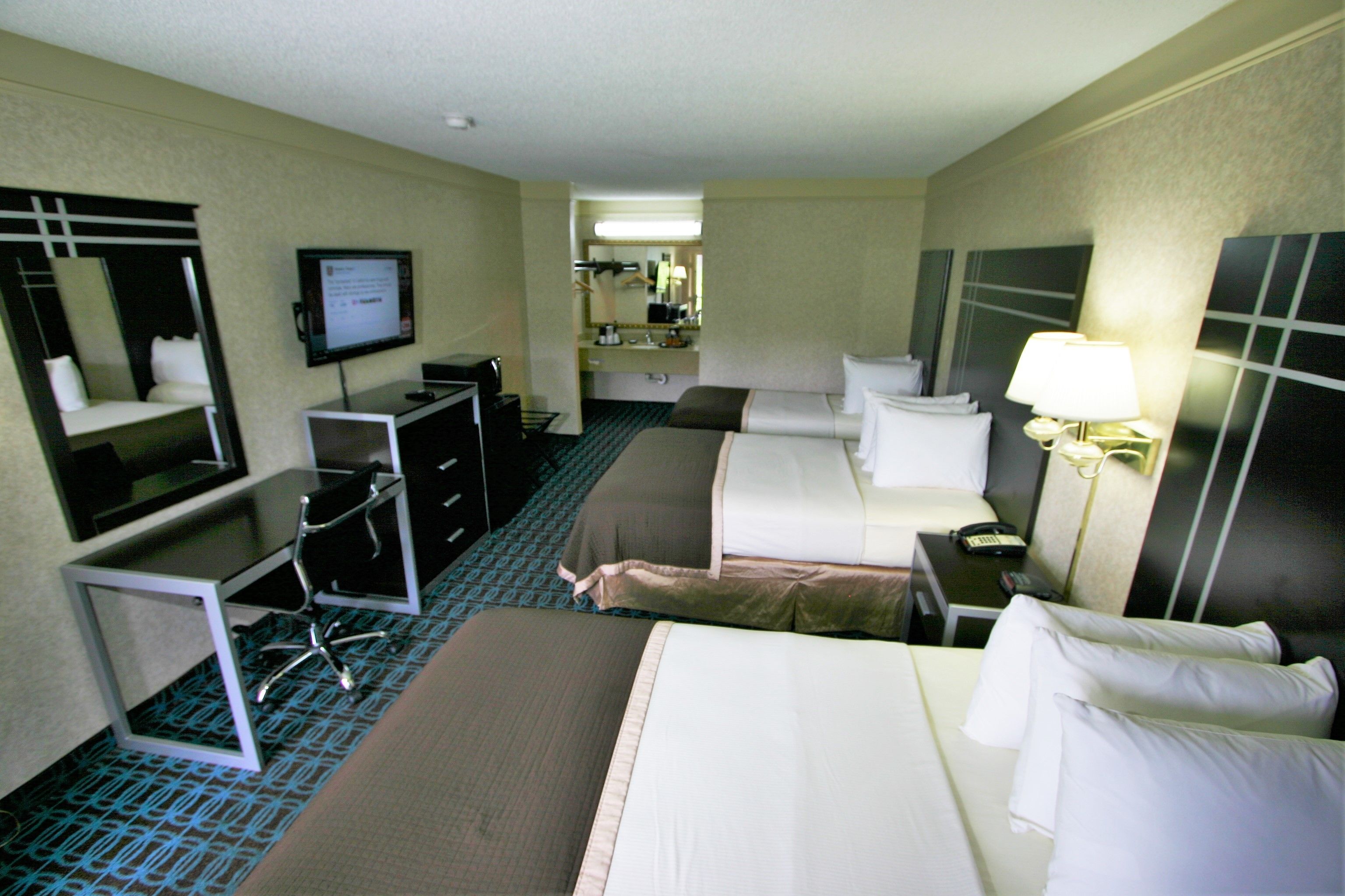 A hotel room with two beds, a desk, a television, and a mirror.