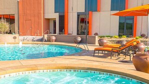 Un área de piscina con sillones de descanso, sombrillas y un jacuzzi pequeño.