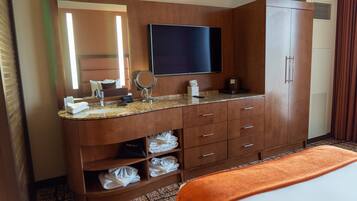 A hotel bathroom with a large mirror, a flat-screen TV, a sink, and a wardrobe.