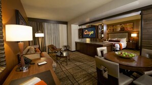 Habitación de hotel con escritorio, sillas, televisor, cama y zona de comedor con frutero.
