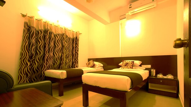 A hotel room with two beds, a small table, a chair, a bedside table, and a curtain with a wavy pattern. - Hotel Udupi Park Inn (Bengaluru)