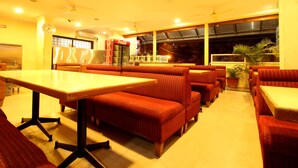 A restaurant with booths and tables, a Coca-Cola refrigerator, and a large window with a view. - Hotel Udupi Park Inn (Bengaluru)