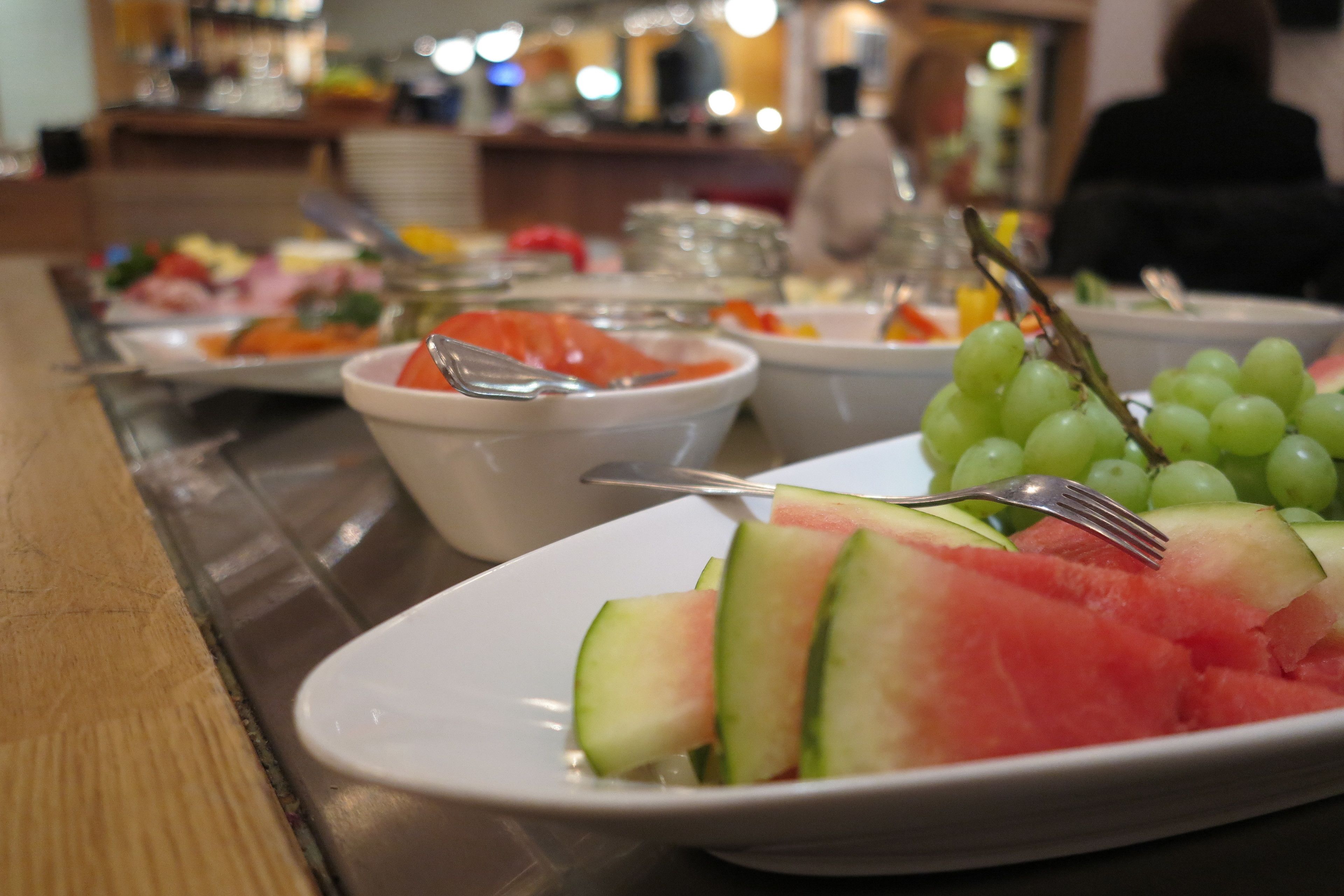 A buffet table with various dishes including watermelon and grapes.
