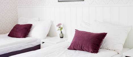 Habitación de hotel con dos camas, ropa de cama blanca y almohadas moradas.