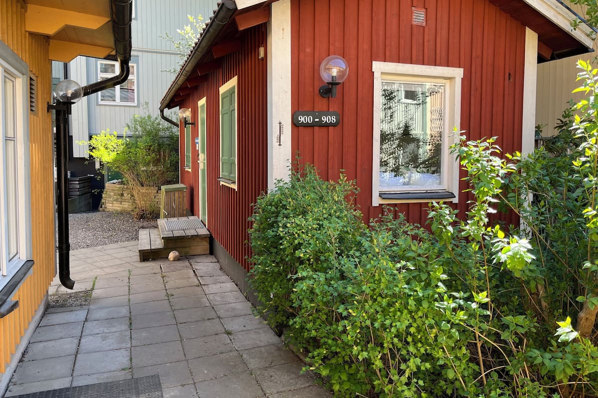 A red wooden building with a number plaque, a window, and a bench outside.