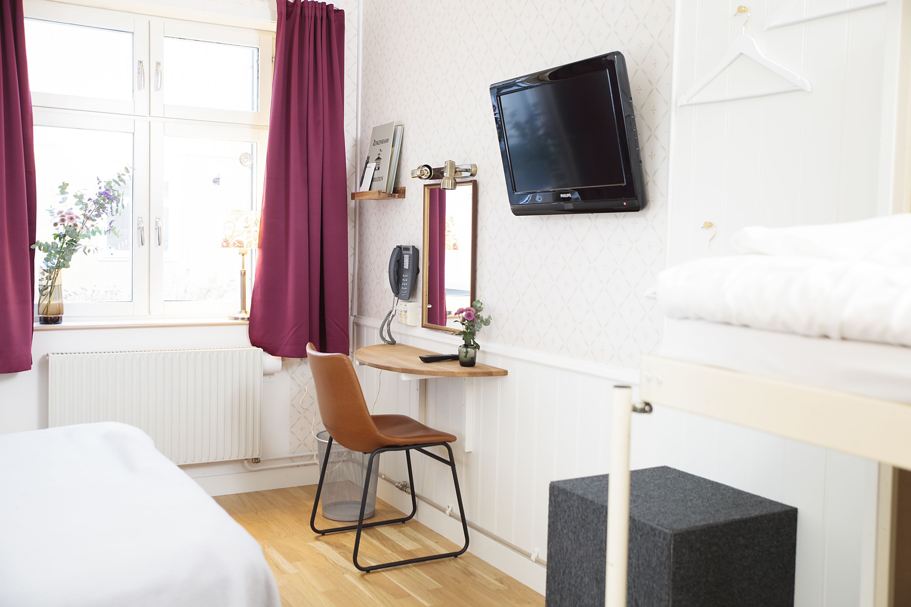 Habitación de hotel con cama, escritorio y silla, televisor, espejo y ventana con cortinas.