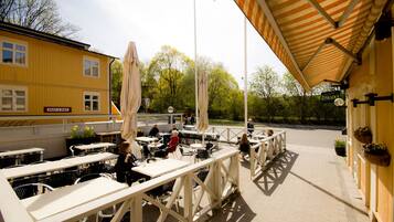 An outdoor cafe with tables and chairs, a yellow building with a 'Rent a Bike' sign, and a covered seating area with umbrellas.