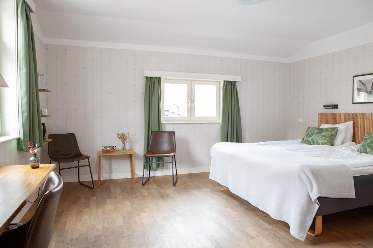 A hotel room with a bed, a chair, a small table, and a window with curtains.