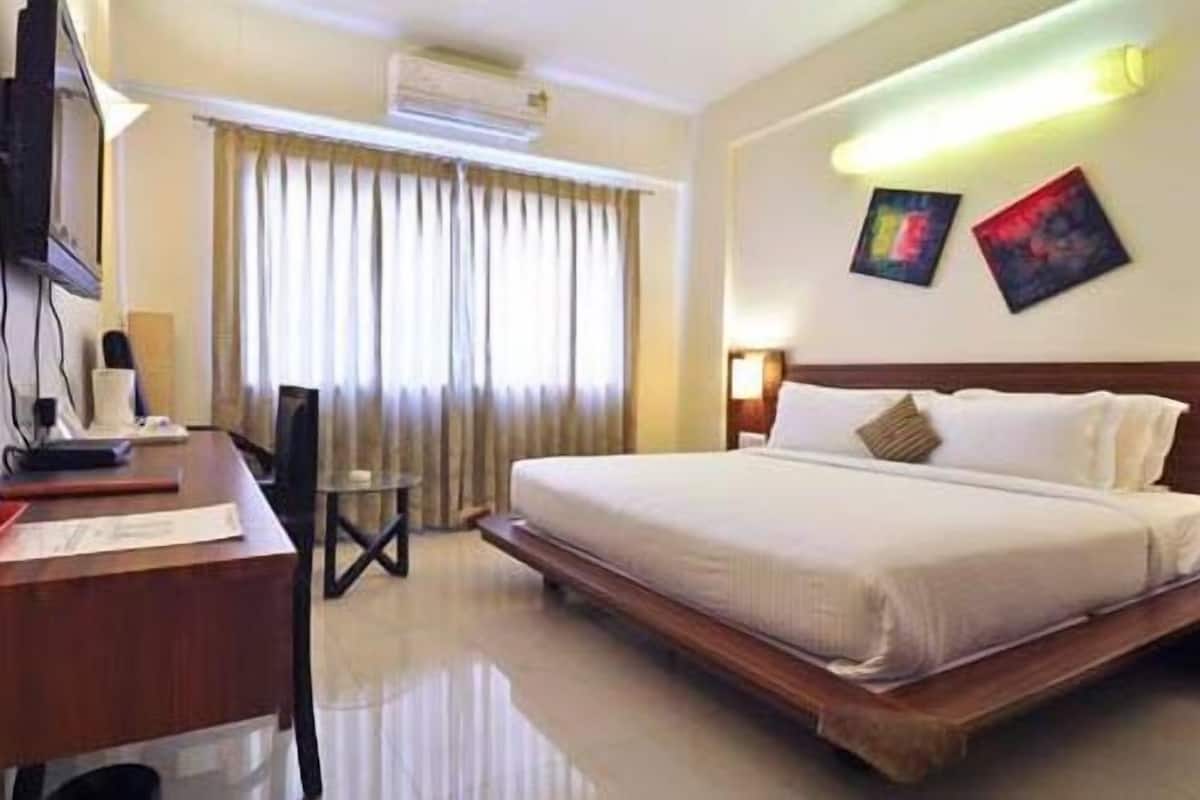 A hotel room with a bed, desk, chair, and artwork on the wall.