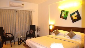 A hotel room with a bed, two chairs, a small table, and a wall-mounted air conditioner. - Hotel Ekaa (Bengaluru)