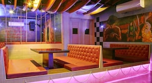 Una habitación con pared estampada de cuadros, un mural y una zona de estar con mesa y bancos acolchados.