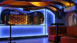A modern bar area with a unique hexagonal light fixture, a red cushioned seating area, and a sign indicating '1428 E. 1st St.' - Hotel Ekaa (Bengaluru)