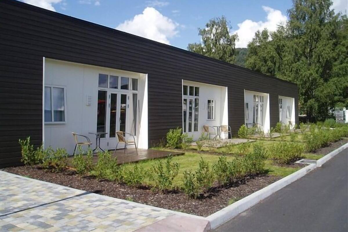 A modern building with three rooms, each with a door and windows. There are outdoor seating areas with chairs and tables.