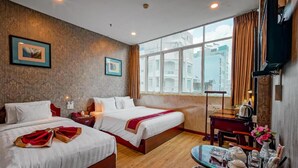 A hotel room with two beds, a desk with a chair, a small table, and a large window with curtains. - Xavier Hotel (Ho Chi Minh City)