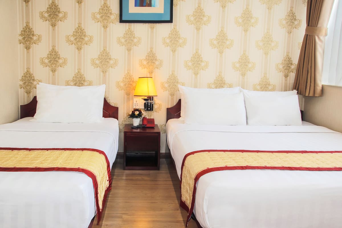 A hotel room with two beds, a nightstand with a lamp, a telephone, and a framed picture on the wall.
