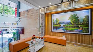 A modern lobby with a large painting, orange seating, and a glass coffee table with decorative items. - Xavier Hotel (Ho Chi Minh City)
