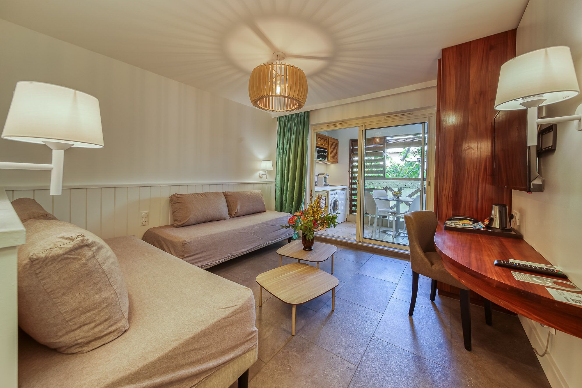 Ein gemütliches Zimmer mit einer Couch, einem kleinen Tisch mit einer Vase, einem Holztisch mit einem Stuhl und einer Glasschiebetür, die zu einem Außenbereich führt.