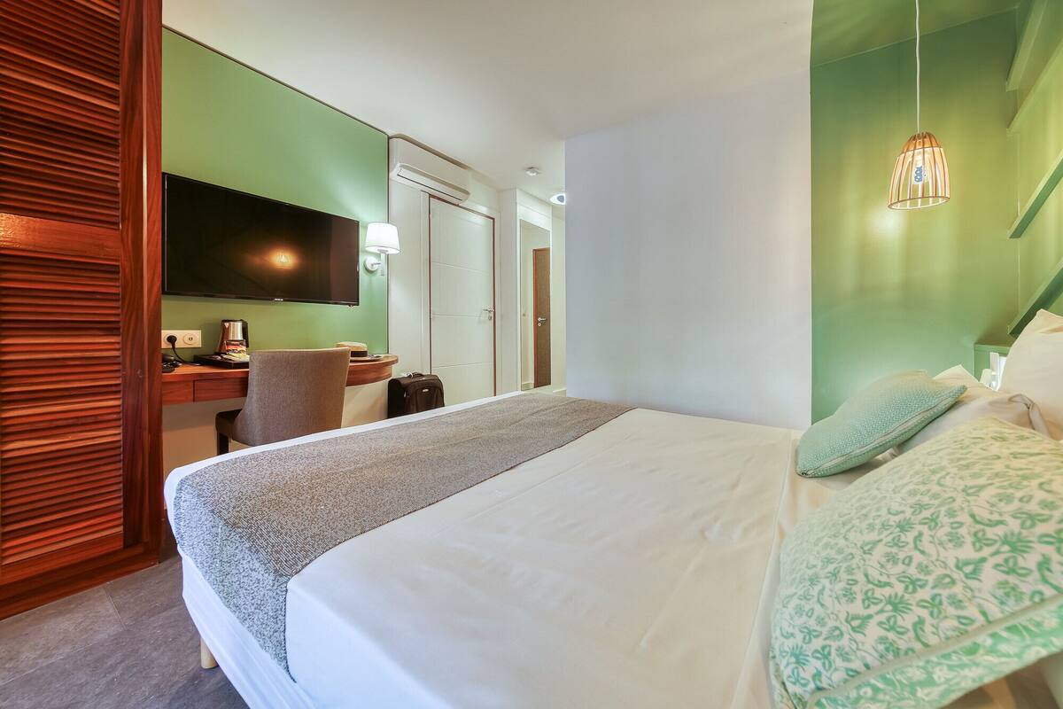 Habitación de hotel con cama, escritorio con silla, televisor y puerta hacia el baño.