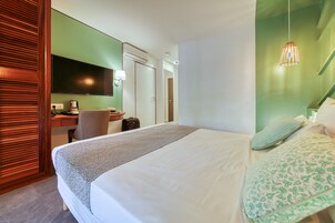 Habitación de hotel con cama, escritorio con silla, televisor y puerta hacia el baño.