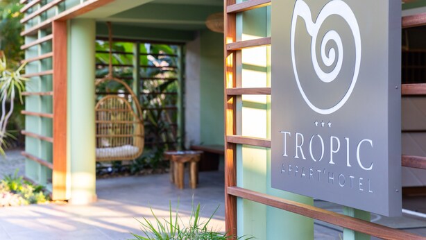 A sign for Tropic Apartment Hotel with a modern design and a wicker chair visible in the background. - Residence Tropic Appart'hotel (Saint-Paul)