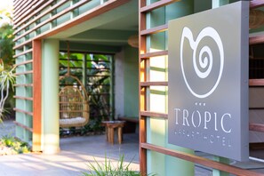 Een bordje voor Tropic Apartment Hotel, met een modern ontwerp en een rieten stoel op de achtergrond zichtbaar.