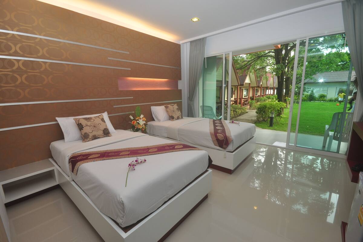 Una habitación de hotel moderna con dos camas, un amplio ventanal corredero a un jardín y un diseño limpio y minimalista.