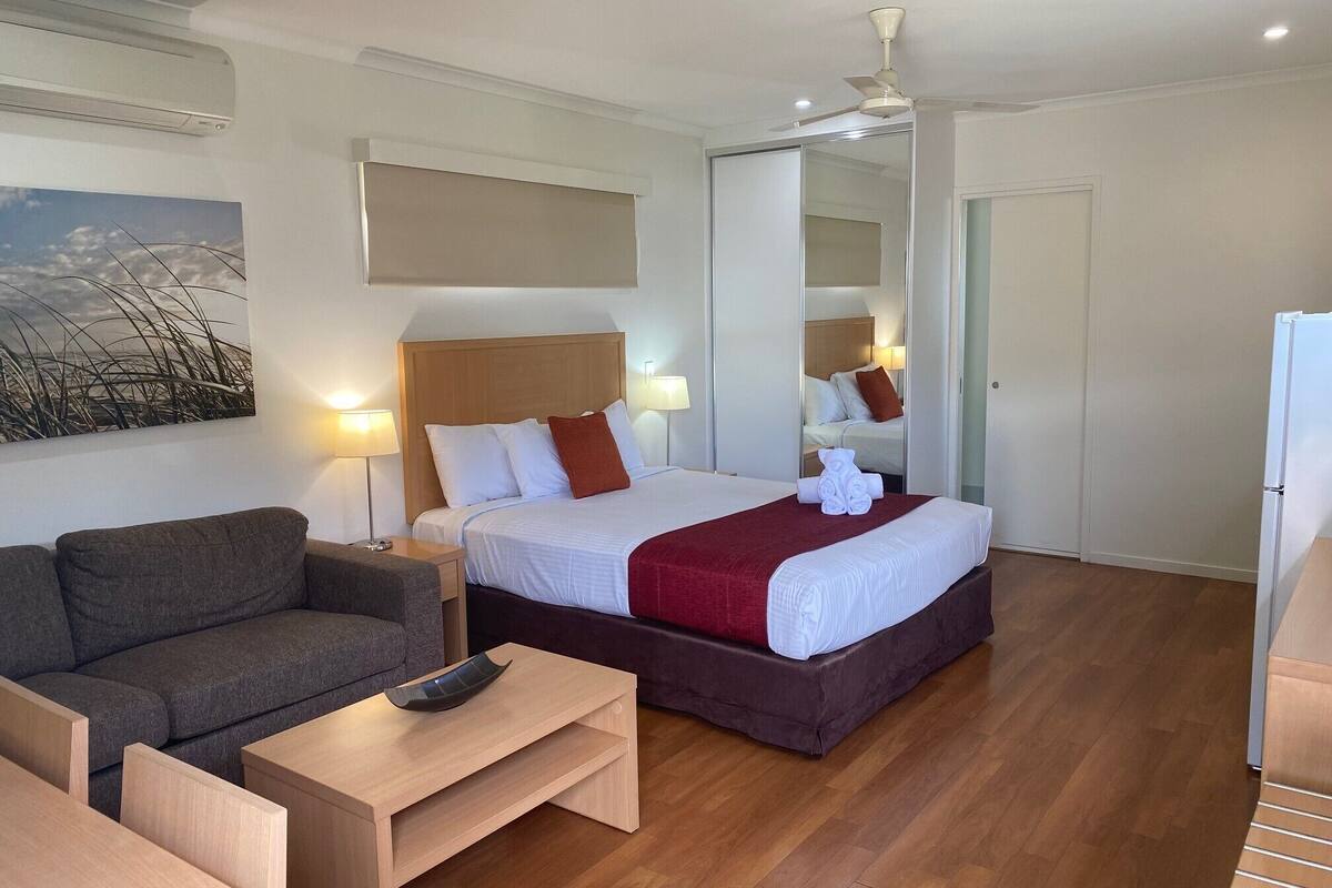 Una habitación de hotel con cama, sofá, una mesita y ventilador de techo.