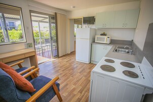 Cocina compacta con estufa, microondas y refrigerador. Hay un comedor con mesa y sillas, y un balcón con vistas a zonas verdes.
