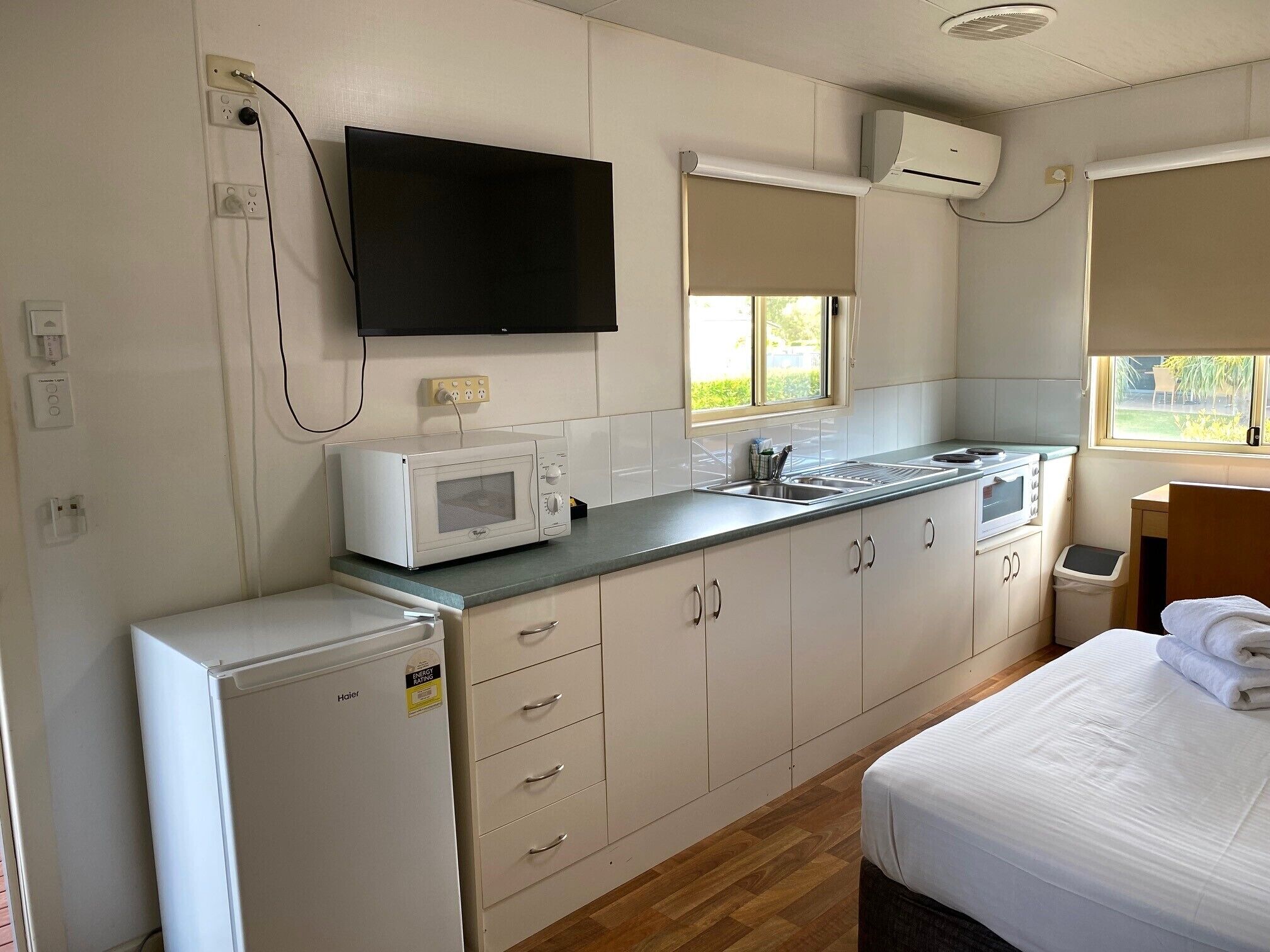A compact kitchenette with a microwave, stove, and sink. There is a bed with a neatly made white duvet.