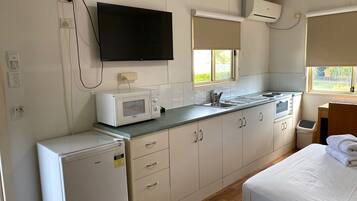 A compact kitchenette with a microwave, stove, and sink. There is a bed with a neatly made white duvet.